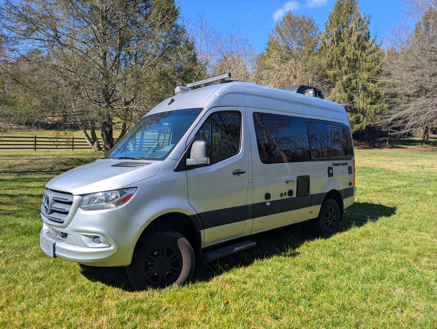 Silver Mercedes-Benz Sprinter camper van RV rental parked on a sunny green field with trees. Ready for adventure.