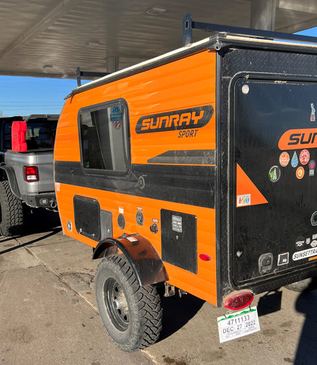 Bright orange Sunray Sport teardrop RV rental, a rugged off-road camper trailer, attached to a Jeep for adventure.