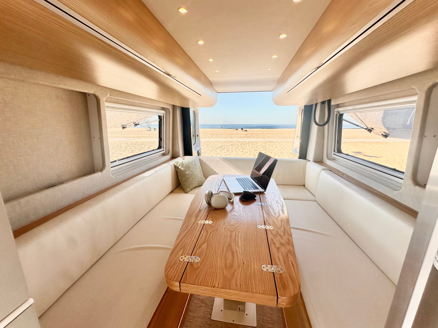 Modern rv rental interior: a bright workspace with a laptop, headphones on a wood table, and a stunning beach view. — photo 5