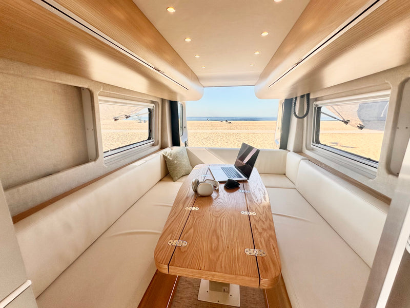 Modern rv rental interior: a bright workspace with a laptop, headphones on a wood table, and a stunning beach view. — photo 5