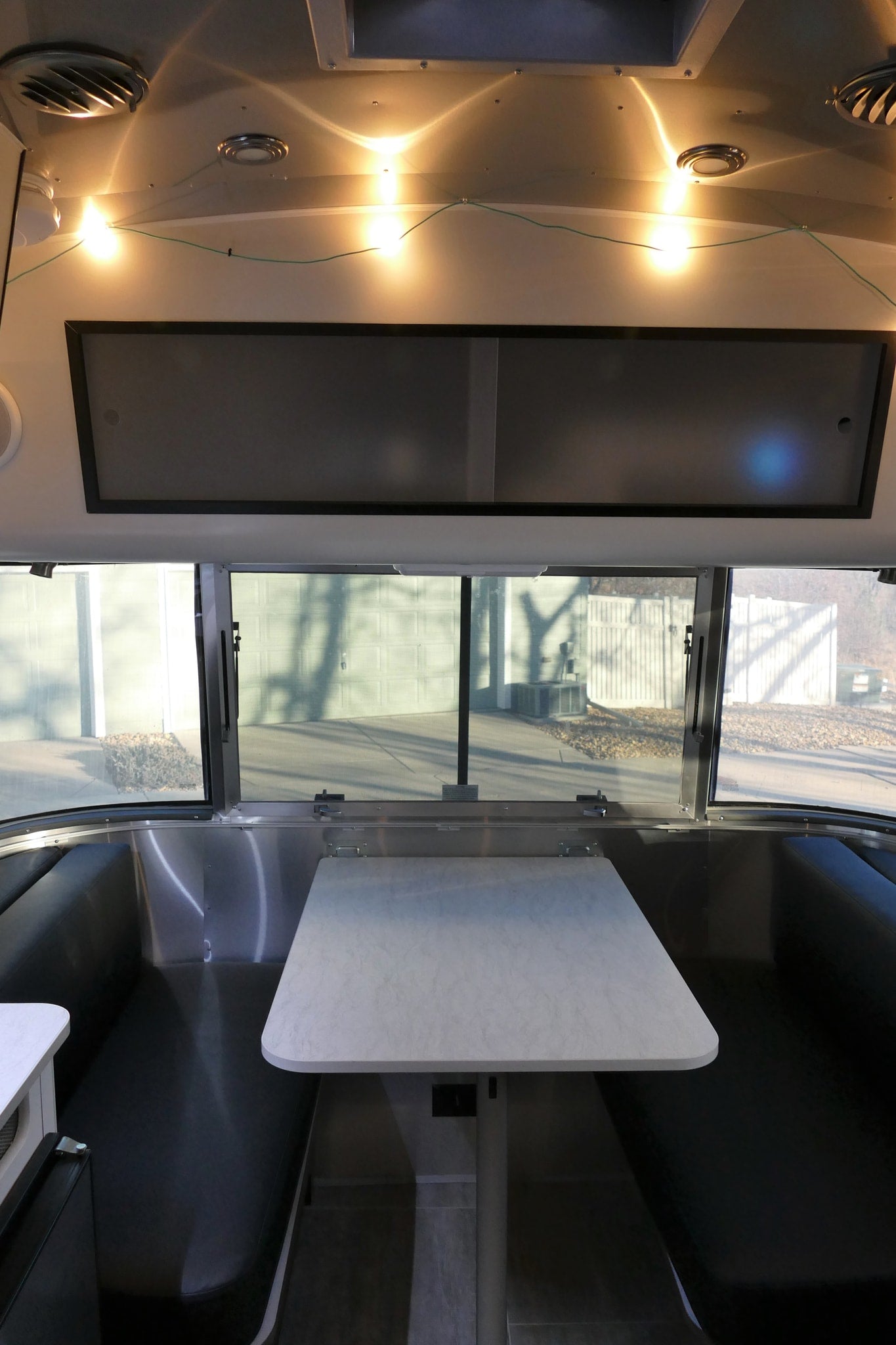 Bright rv rental dinette with black benches, a white table, overhead cabinets, and large scenic windows. — photo 17