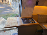 Cozy RV rental kitchen featuring a gas stovetop, extendable counter, and tiled backsplash, with outdoor views.