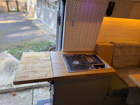 Cozy RV rental kitchen featuring a gas stovetop, extendable counter, and tiled backsplash, with outdoor views.