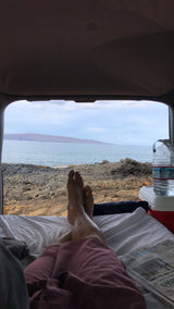 Coastal comfort: Feet up inside an RV rental, enjoying the serene ocean view and distant island.
