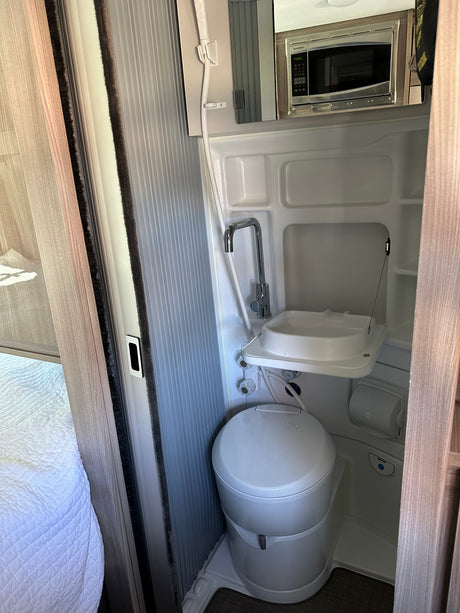 Compact RV rental wet bath with white toilet, sink, and shower. Microwave installed overhead.