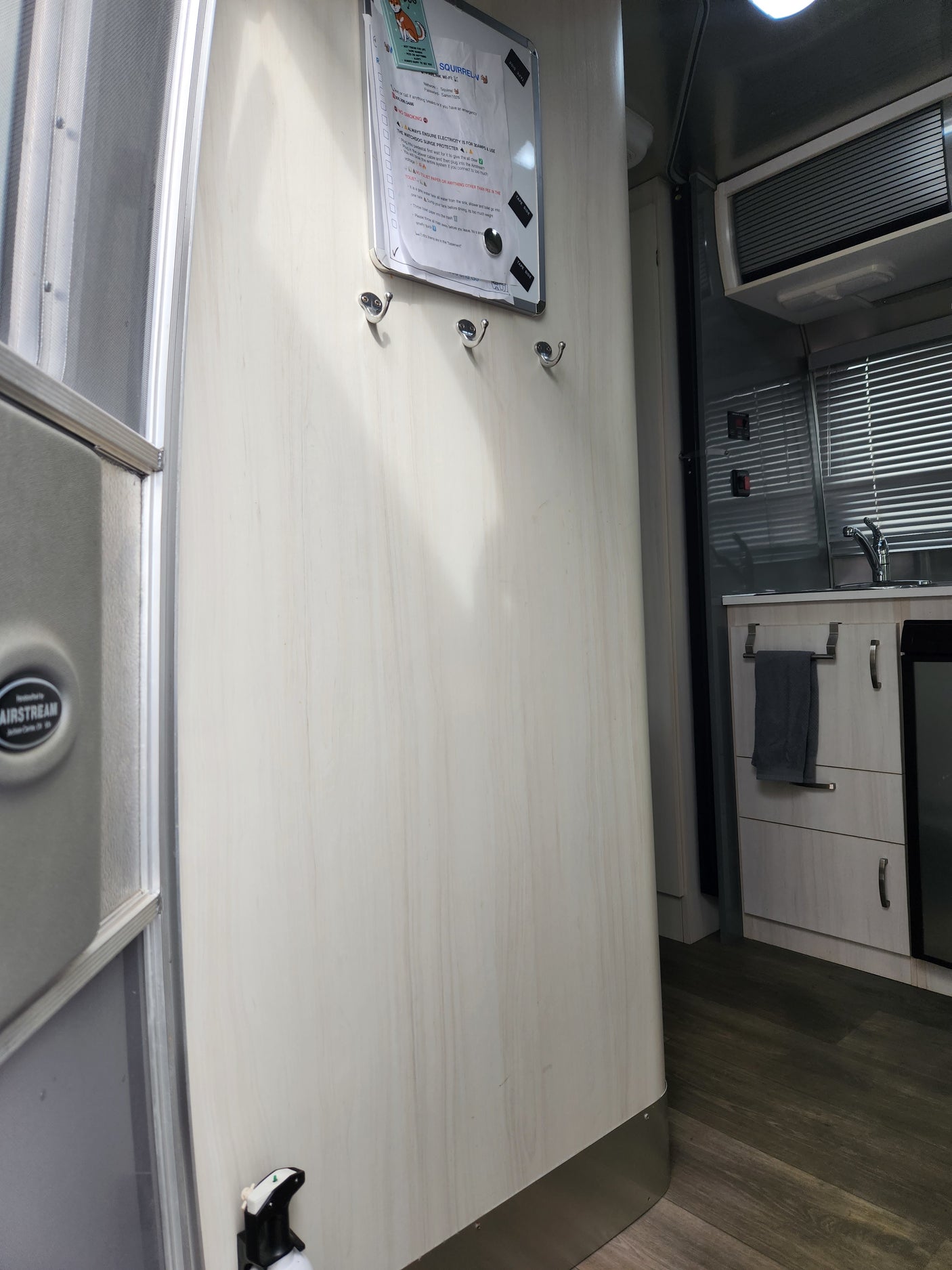 Inside an Airstream rv rental: a compact kitchen, coat hooks, and a whiteboard with guest instructions, near the entrance.