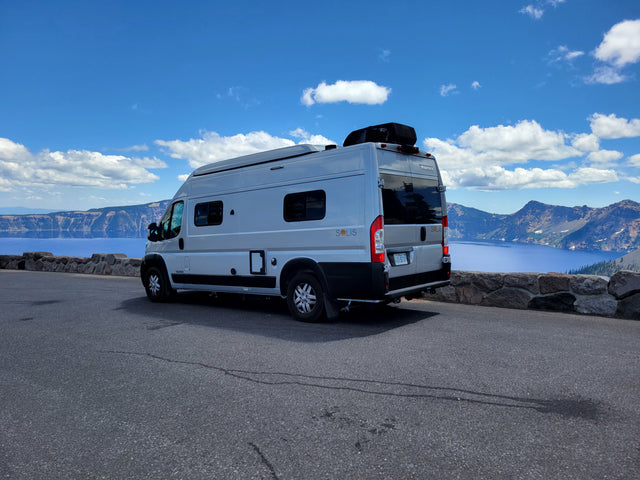 This RV rental, a Winnebago Solis, offers breathtaking views of Crater Lake's deep blue water and surrounding mountains.