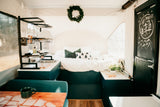 Cozy RV rental interior featuring a comfy bed, compact kitchen with sink, and a "Happy Campers" chalkboard door.