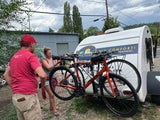 Setting up for adventure: Two people with bikes attached to a white teardrop rv rental, featuring "BIG COMFORT!" branding.