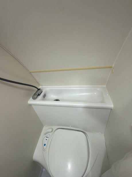 RV rental's compact bathroom features a toilet with an integrated sink and a flexible shower head for small spaces.