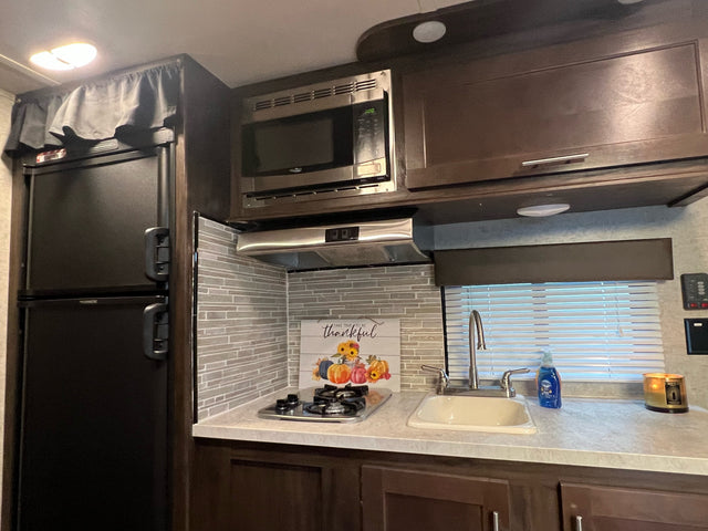 RV rental kitchen showcasing a fridge, microwave, stovetop, sink, and fall decor with mosaic backsplash.