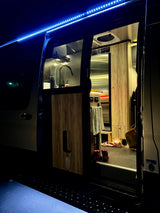 Cozy rv rental interior at night, featuring bright blue exterior LEDs, a lit kitchen, and an open camper van side door.