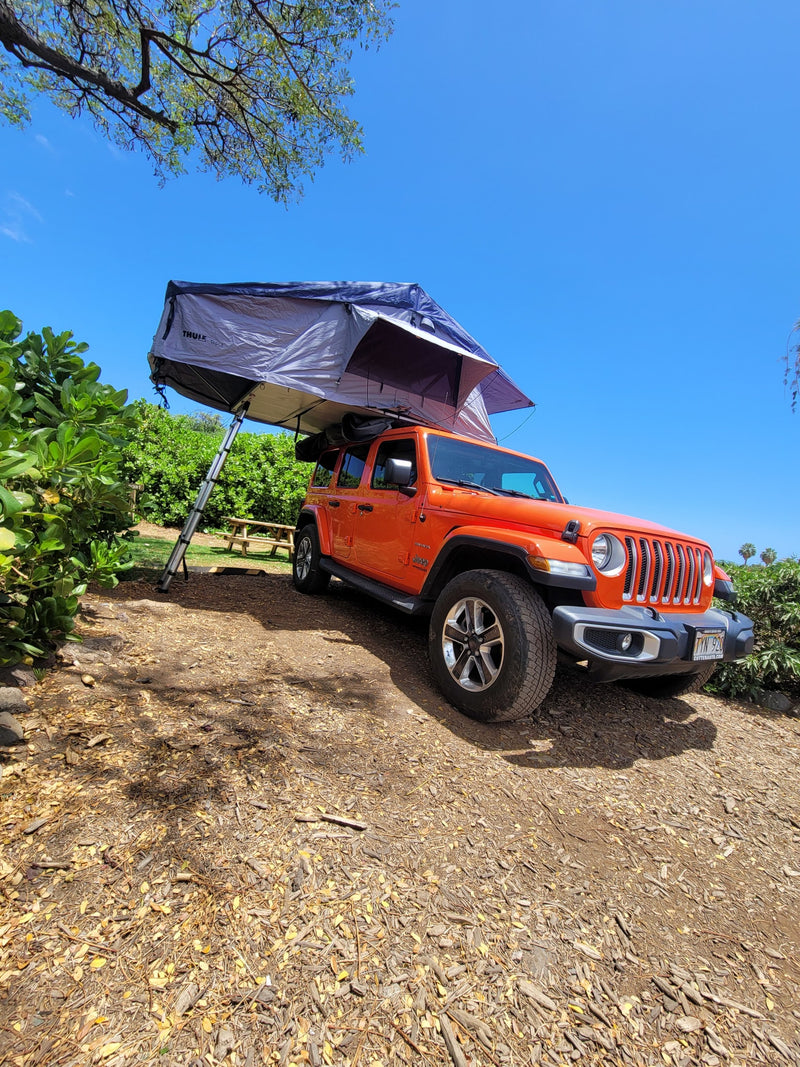An orange Jeep with a rooftop tent, ideal for an RV rental, parked in a scenic outdoor camping spot under a blue sky. — photo 18