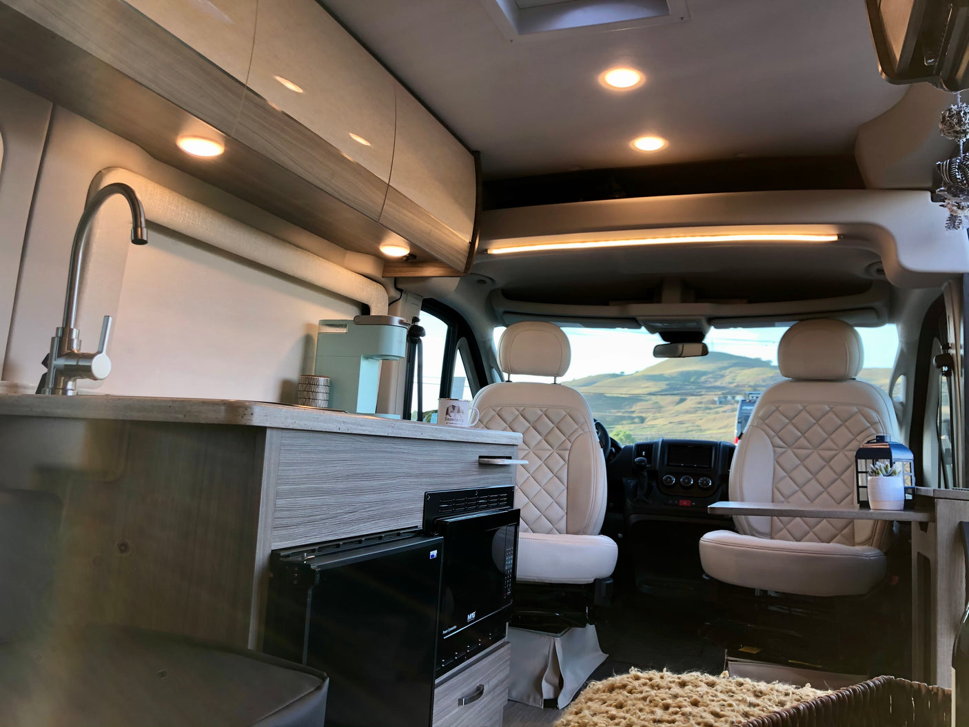 Spacious campervan RV rental: kitchenette with sink, Keurig, quilted front seats, and scenic mountain views out the windshield.