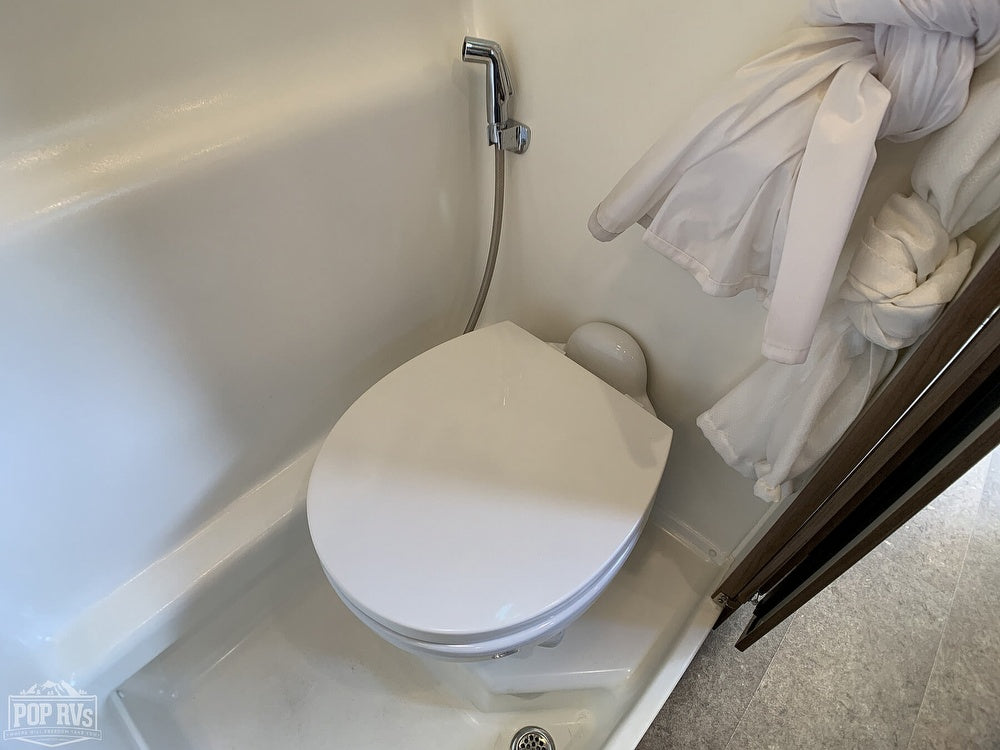 RV rental's compact white wet bath. This functional space includes a toilet and a wall-mounted shower head for efficient use.