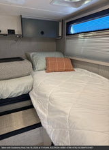 Cozy RV rental bedroom featuring a comfortable bed with soft bedding, pillows, and a window with blinds showing bright blue sky.