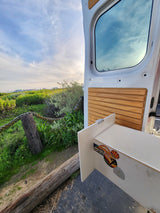 RV rental van door open to lush outdoor view, revealing interior wood paneling and travel stickers.