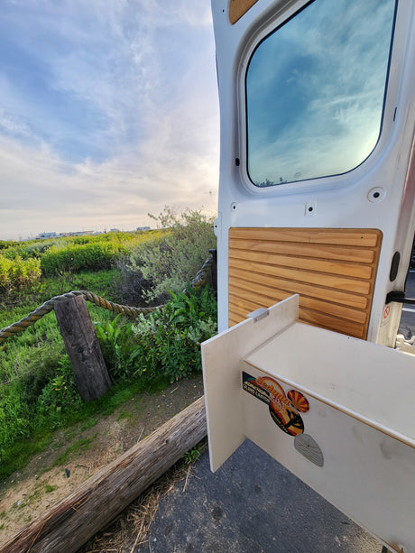 RV rental van door open to lush outdoor view, revealing interior wood paneling and travel stickers.