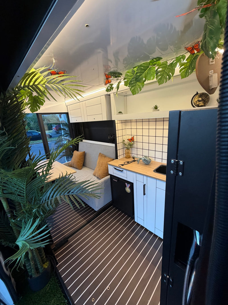 Tropical-themed RV rental interior featuring a kitchenette, seating, and lush plants. Perfect for a cozy getaway. — photo 10