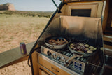 Enjoying an RV rental outdoor kitchen, preparing a camp meal with meat & veggies on the stove, cold beer ready. Adventure awaits!