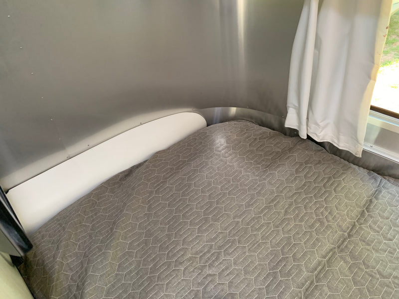  is parked on a gravel lot under a clear sky.|Cozy RV rental sleeping area features quilted grey bedding — photo 7