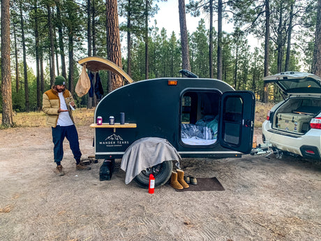 Man at a serene forest campsite with his teardrop camper, perfect for an RV rental adventure.