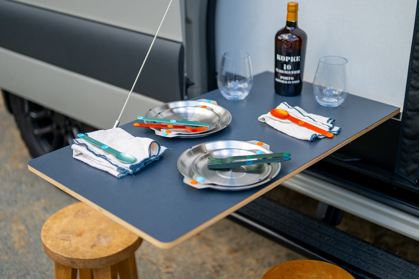 RV rental outdoor dining: Pop-out table with Porto wine, reusable plates, colorful cutlery, and napkins, ready for a meal.