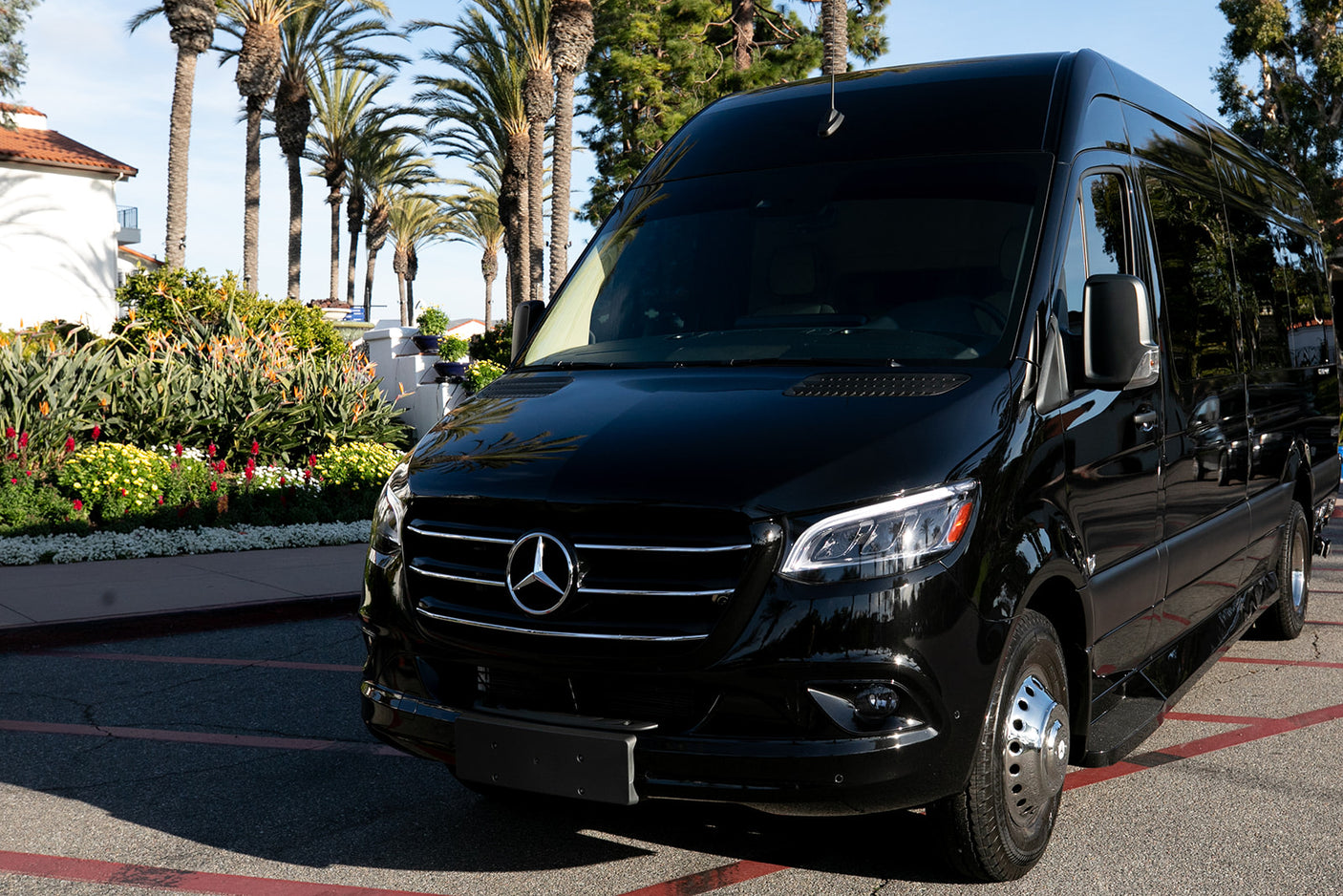 Black Mercedes-Benz Sprinter van, perfect for a luxury RV rental experience, parked by lush gardens and palm trees.