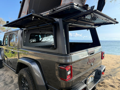 Gray Jeep Gladiator with open camper shell and Roofnest rooftop tent, an ultimate RV rental for beach adventures.