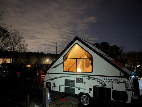Visually impaired: An illuminated A-frame "Flagstaff Classic" rv rental at a night campsite with power hookup.