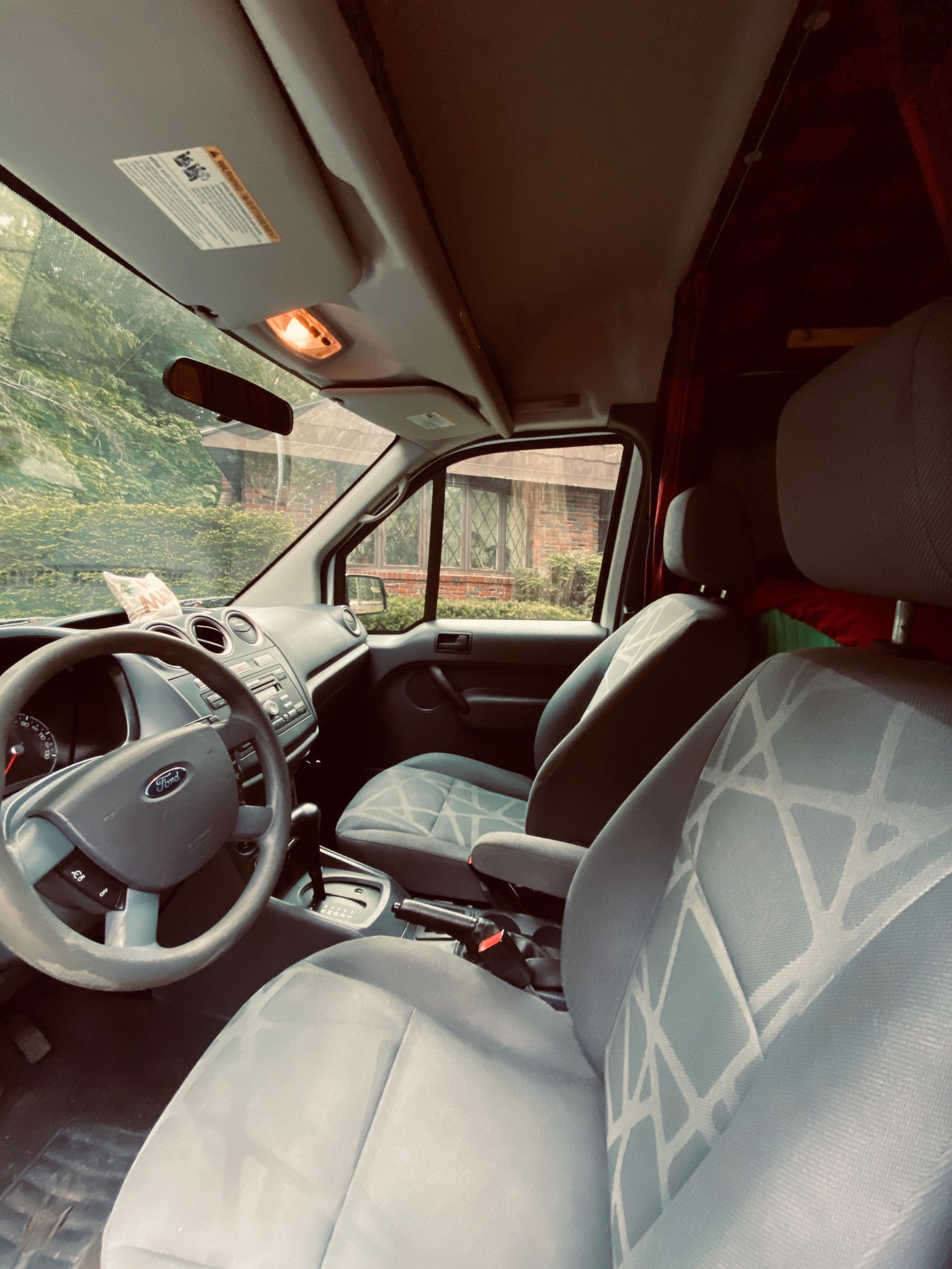 Step inside this RV rental's Ford van interior, showcasing the steering wheel, dashboard, and light-colored front seats.