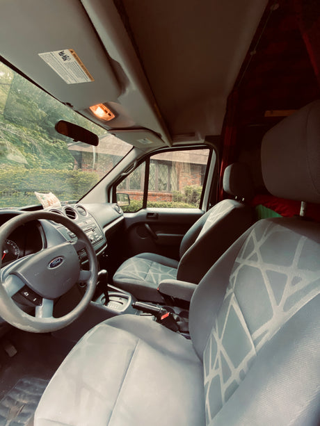 Step inside this RV rental's Ford van interior, showcasing the steering wheel, dashboard, and light-colored front seats.