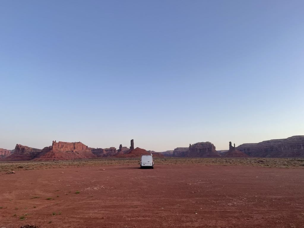 An RV rental parked in a vast, red desert with towering sandstone formations under a clear blue sky, perfect for adventure. — photo 2