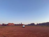 An RV rental parked in a vast, red desert with towering sandstone formations under a clear blue sky, perfect for adventure.