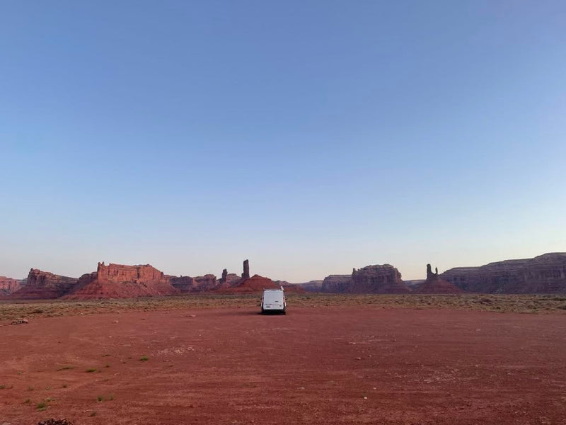 An RV rental parked in a vast, red desert with towering sandstone formations under a clear blue sky, perfect for adventure. — photo 2