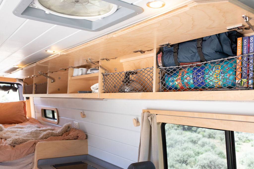 Cozy RV rental interior showcasing functional overhead wood cabinets with netting storage, a comfortable bed, and compact design.