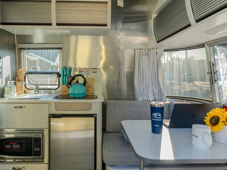 Bright Airstream RV rental interior: modern kitchen, dining area with laptop, and comfy seating. Ideal for travel.