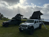 Two Jeep Gladiator RV rentals with rooftop tents by the ocean. Perfect for an off-road camping adventure on grassy terrain.