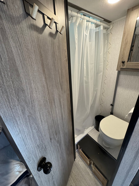 RV rental's compact bathroom features a shower, toilet, and storage step, with convenient wall hooks.