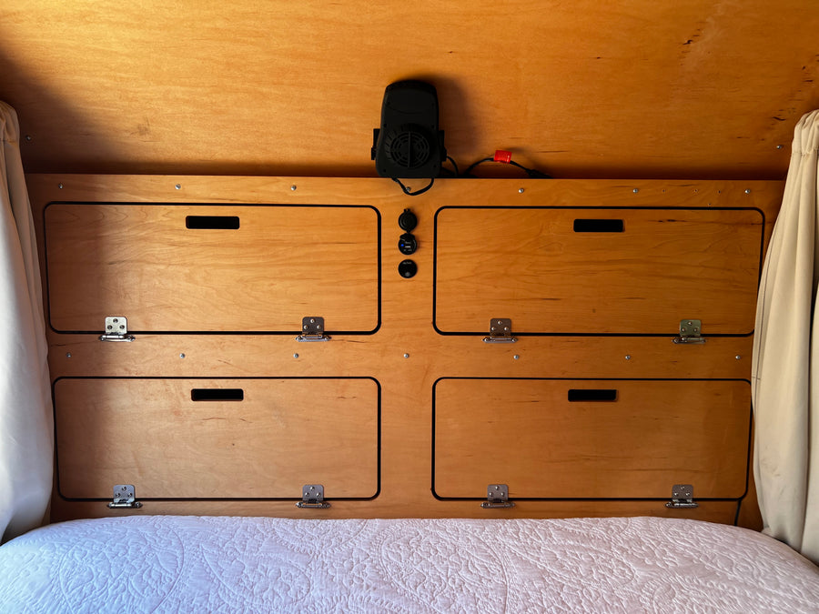 Cozy wooden interior of an RV rental, showing built-in storage, fan, & charging ports above a bed.