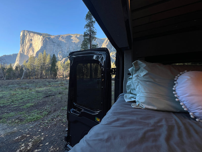 Cozy RV rental bed with an open door showcasing Yosemite's iconic El Capitan & forests under a bright blue sky. Perfect van life! — photo 5