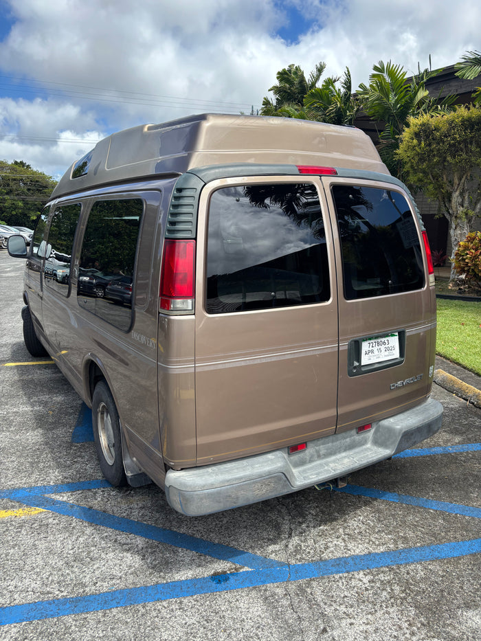 Tan Chevrolet Discovery camper van, likely an RV rental, parked with its distinctive high roof.