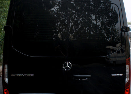 Black Mercedes-Benz Sprinter 3500 van, great for **rv rental**, rear view with reflections of trees and an RV.