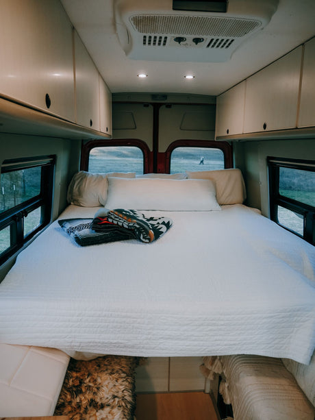 Cozy RV rental bedroom with spacious bed, overhead storage, and scenic views. Perfect for your next van life adventure!