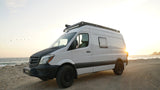 White Mercedes Sprinter camper van parked on a beach at sunset, perfect for an RV rental adventure.