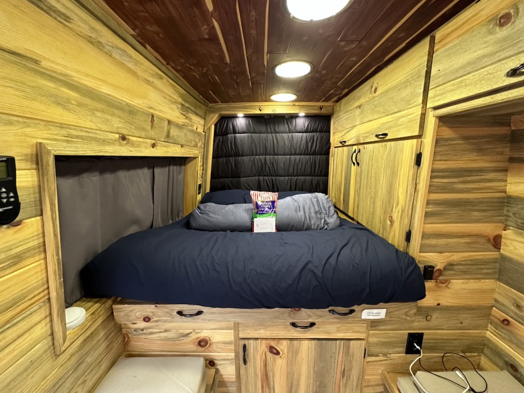  and a convenient pull-out table.|Experience an RV rental. Cozy bed and blankets by a large window with a dense — photo 9
