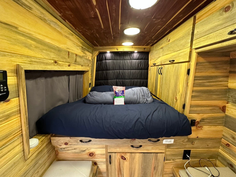  and a convenient pull-out table.|Experience an RV rental. Cozy bed and blankets by a large window with a dense — photo 9