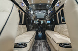 Spacious RV rental interior featuring plush cream leather seating, entertainment screens, and rich wood trim.