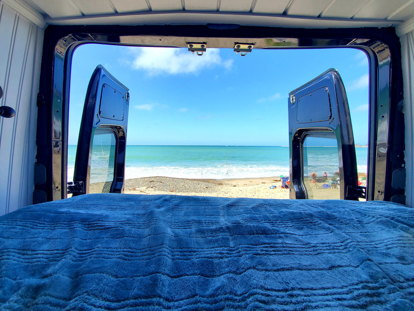 Waking up to this ocean view from an RV rental bed. Open van doors frame a serene beach scene.