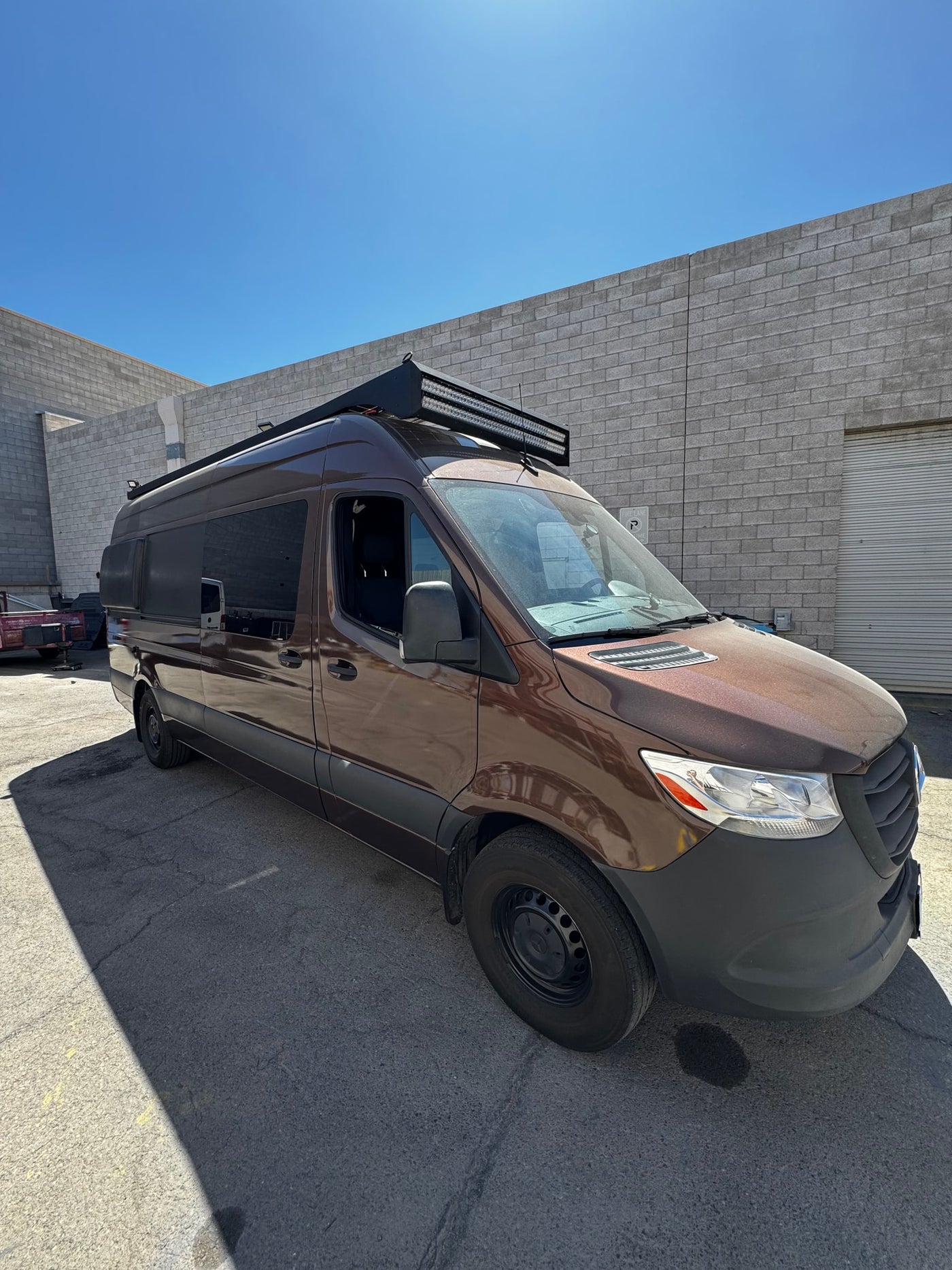 Brown Sprinter camper van, ideal for RV rental, parked outside a building under a clear blue sky. — photo 9